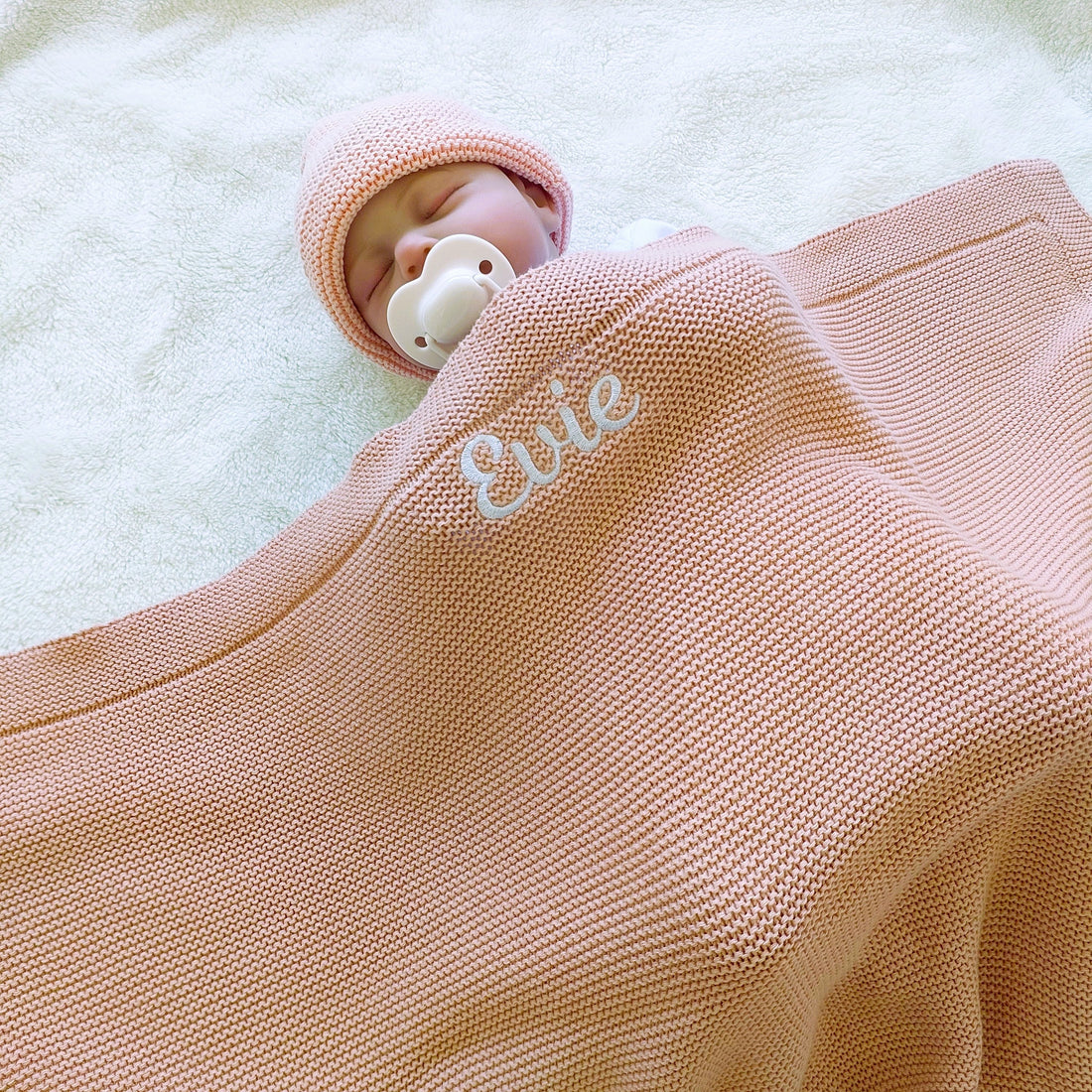 Newborn baby sleeping under a pink knitted blanket embroidered with the name Evie
